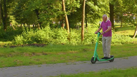 Senior-stylish-man-grandfather-tourist-riding-electric-scooter-in-park,-modern-life-after-retirement