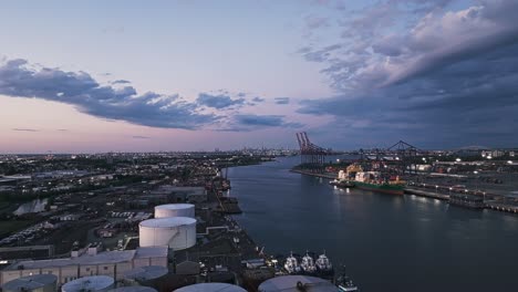 Panoramic-aerial-establishing-view-of-harbor-port-with-storage-tanks-and-large-transit-cranes-at-dusk