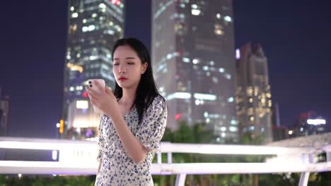 Close-up-beautiful-lonely-girl-playing-with-looking-at-mobile-phone-on-the-overpass-under-high-rise-building-at-night