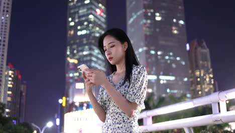 Close-up-beautiful-lonely-girl-playing-with-looking-at-mobile-phone-on-the-overpass-under-high-rise-building-at-night