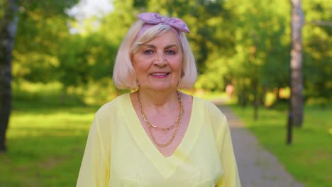 Cheerful-lovely-senior-old-gray-haired-grandmother-in-casual-yellow-blouse-on-summer-park-background