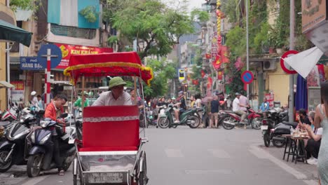 Old-man-riding-an-empty-red-tricycle-on-Hanoi-street,-traffic-background,-colorful-road