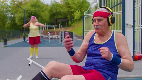 Senior-old-grandfather-with-headphones-listening-music-from-mobile-phone-on-playground-and-dancing