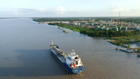 Aerial:-Oil-tanker-ship-sailing-to-dock-in-Suriname-river,-refinery-in-background-with-clear-sky