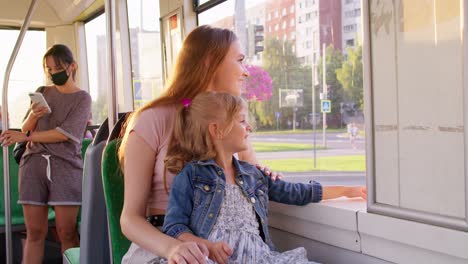 Family-rides-in-public-transport,-woman-with-little-child-girl-sit-together-and-look-out-window-tram