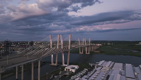 Drone-orbits-above-suspension-concrete-bridges-with-port-access-and-harbor-cranes-in-background-at-dusk