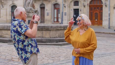 Abuelo-Turista-Anciano-Tomando-Fotografías-De-La-Abuela-Con-Una-Cámara-Retro-En-La-Antigua-Ciudad-De-Verano