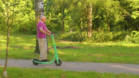 Caucasian-old-gray-haired-senior-stylish-man-grandfather-riding-electric-scooter-in-summer-park