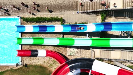 Super-slow-motion-aerial-footage-of-man-sliding-vibrant-multi-colored-water-slide-at-aquapark