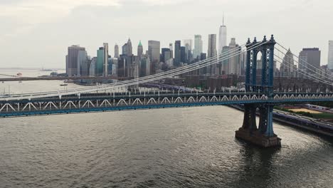 Luftaufnahme-Von-Der-Manhattan-Bridge,-Die-Sich-Neigt,-Um-Die-Skyline-Von-New-York-Mit-Gebäuden-Und-Booten-Auf-Dem-Fluss-Freizugeben