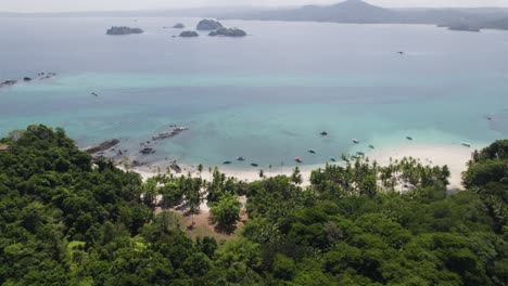 Luftaufnahme-Eines-Tropischen-Strandes,-Umgeben-Von-Dichtem-Grün,-Mit-Klarem-Blauen-Wasser-Und-Entfernten-Inseln,-Die-Einen-Ruhigen-Küstenurlaub-Bieten