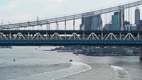 Aerial-pan-right-along-Manhattan-bridge-with-boats-and-ferries-driving-along-East-river-in-New-York-City