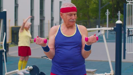 Senior-man-grandfather-doing-training-weightlifting-exercising-with-dumbbells-on-playground-in-park