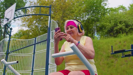 Mujer-Mayor-Después-Del-Entrenamiento-Deportivo-Escuchando-Música-En-El-Patio-De-Recreo,-Celebra-La-Victoria-Haciendo-Un-Gesto-De-Ganador