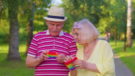 Stylish-senior-grandmother-grandfather-playing-squeezing-anti-stress-toy-simple-dimple-game-in-park