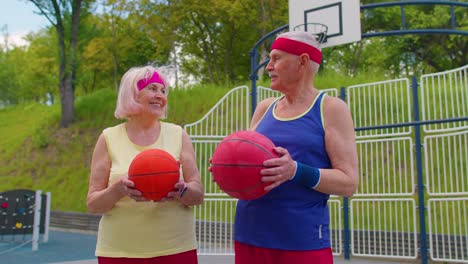 Active-senior-basketball-team-man-woman-playing-game-with-ball,-smiling-looking-at-camera-at-stadium