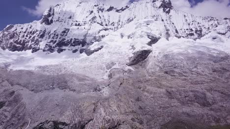 Atemberaubende-Luftaufnahme-Eines-Leuchtend-Türkisfarbenen-Sees,-Umgeben-Von-Steilen,-Schneebedeckten-Berggipfeln-Mit-Gletschern-Und-Felsigen-Klippen-Unter-Einem-Strahlend-Blauen-Himmel