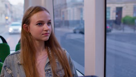 Attraktive-Junge-Frau-Als-Passagierin-Im-Modernen-öffentlichen-Bus-Oder-In-Der-Straßenbahn,-Blick-Aus-Dem-Fenster