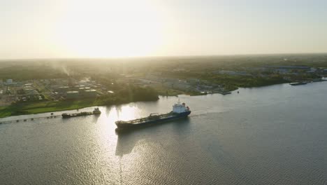 Aerial:-Oil-tanker-ship-sailing-to-dock,-Suriname-river,-sunset-in-background,-drone-following