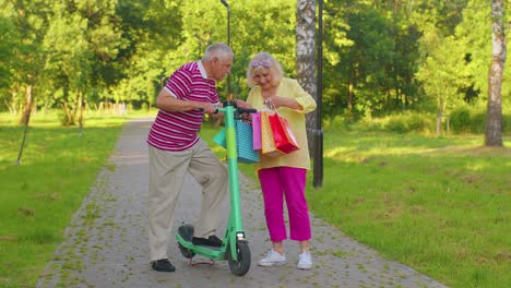 Senior-stylish-couple-grandmother,-grandfather-after-shopping-with-bags-using-scooter-for-riding