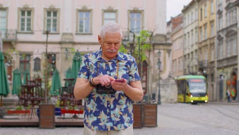 Elderly-stylish-tourist-man-looking-for-way-find-route-using-smartphone-in-old-town-Lviv,-Ukraine