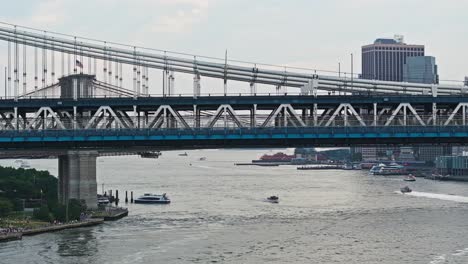 Drone-pan-follows-along-Manhattan-bridge-with-Brooklyn-bridge-waterfront-park-below,-aerial