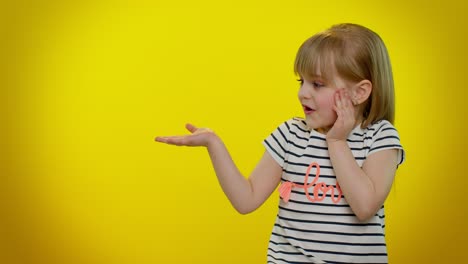 Little-kid-child-girl-showing-thumbs-up-and-pointing-at-left-on-blank-space-on-yellow-background