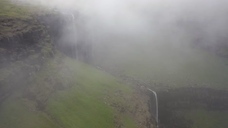 Fossá-Waterfall,-aerial-reveal-behind-coastal-cliffs-and-mist-in-Faroe-Islands