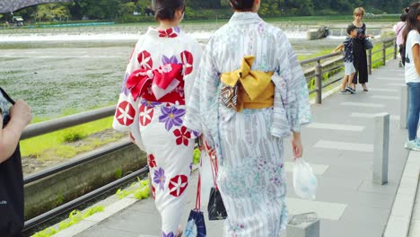 Dos-Hermosas-Chicas-Caminando-Por-Un-Puente-Al-Lado-De-Un-Río-En-Kioto,-Japón,-Cámara-Lenta-4k