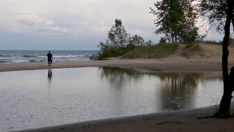 Woman-walking-on-beach-after-a-storm-with-pond-created-by-rain-in-foreground