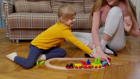 Mother-playing-with-child-kid-daughter-riding-toy-train-on-wooden-railroad-blocks-board-game-at-home