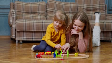 Mother-playing-with-child-kid-daughter-riding-toy-train-on-wooden-railroad-blocks-board-game-at-home