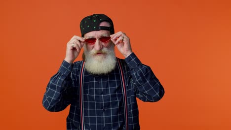 Playful-happy-elderly-bearded-man-in-sunglasses-and-cap-blinking-eye,-looking-at-camera-with-smile