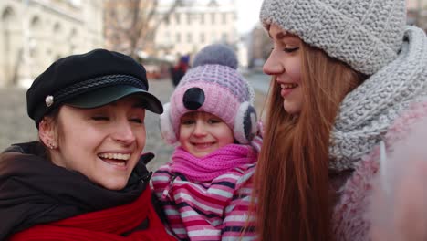 Sisters-tourists-taking-selfie,-posing,-making-video-conferencing-on-mobile-phone-with-child-girl