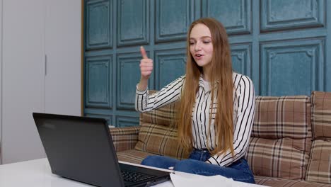 Young-business-woman-sitting-at-workplace-home-office,-making-video-call-on-laptop-shows-thumbs-up