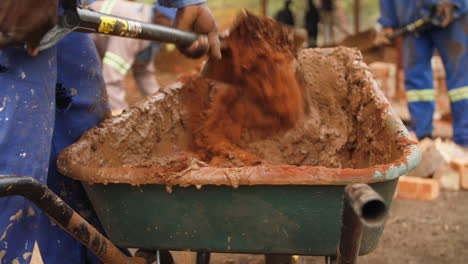 Bauarbeiter-Im-Blauen-Overall-Mischt-Sand-Und-Zement-In-Einer-Schubkarre-Auf-Der-Baustelle