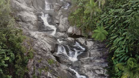 Flying-up-rocky-waterfall-with-dense-forest-with-cracks-and-fast-flowing-water