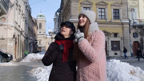 Dos-Mujeres-Turistas-Sonrientes-Caminando-Juntas-Por-Las-Calles-De-La-Ciudad,-Una-Pareja-Familiar-Hablando,-Abrazándose