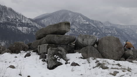 A-girl-climbs-onto-boulders-with-snowy-mountains-around-her