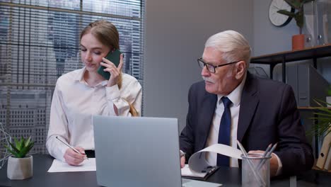 Senior-businessman-company-director-working-on-laptop-computer-in-office,-secretary-talking-on-phone