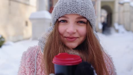 Stylish-woman-traveler-with-hot-drink-in-cup-looking-around-through-city-street-during-vacations