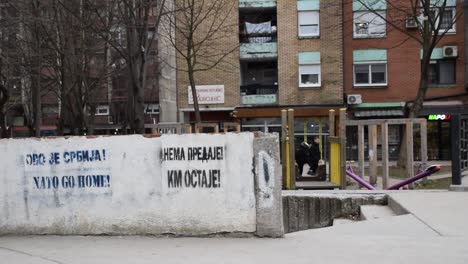 Streetview-with-people-in-north-Mitrovica,-Kosovo,-with-nationalistic-graffiti