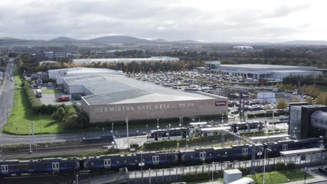 Una-Toma-Aérea-Del-Centro-Comercial-Hermiston-Gate,-Con-Un-Tren-Llegando-Y-Un-Tranvía-Saliendo-De-La-Estación-De-Al-Lado-|-Edimburgo,-Escocia-|-4k-A-30-Fps