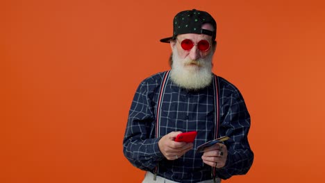 Senior-old-stylish-bearded-man-using-credit-bank-card-and-smartphone-purchases-online-shopping