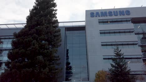 Samsung-Research-America-SRA-campus-in-Silicon-Valley-bottom-up-view-with-green-pine-trees-landscape-under-overcast-sky