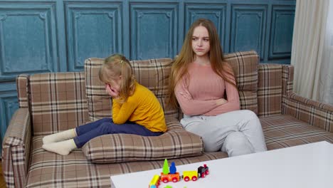 Unhappy-stressed-woman-and-angry-child-girl-sister-ignoring-each-other-sitting-on-sofa-after-quarrel