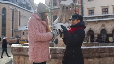 Two-smiling-women-tourists-traveling-together,-drinking-hot-tea,-coffee-from-thermos-on-city-street