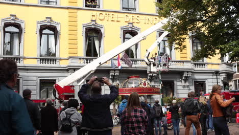 Neugierige-Menschen-Beobachten,-Wie-Die-Feuerwehr-Mit-Einem-Mechanischen-Kran-Einen-Patienten-Auf-Einer-Trage-Aus-Einem-Hotelzimmer-Im-Zweiten-Stock-In-Den-Haag-Im-Hotel-Des-Indes-Entfernt