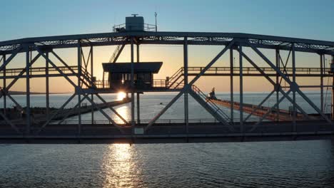 Aerial-view-of-sun-beams-through-metal-framework-of-lift-bridge-over-harbor---drone-tracking-shot-Lake-Superior-Duluth,-Minnesota