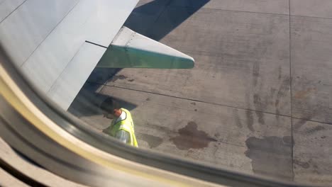 View-from-aircraft-window-out-to-wing---view-of-technician,-mechanic-checking-pre-flight-on-tarmac-runway